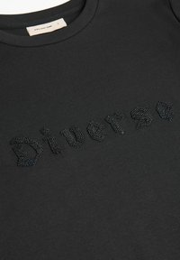 Czarna bawełniana koszulka z teksturowanym czarnym napisem "Diverse" o gładkim wykończeniu i okrągłym dekoltem.