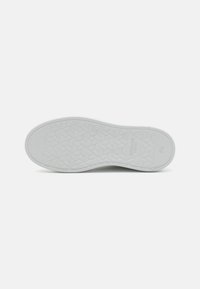 Semelle de chaussure en caoutchouc blanc avec un motif géométrique texturé et un bord lisse. Présente un détail de marque imprimé près du talon.