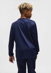 Marinblå långärmad sporttröja med slät textur. Har rund halsringning och matchande marinblå byxor synliga längst ner.