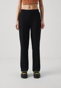 Černé, volné kalhoty vyrobené z měkkého materiálu, s vysokým pasem a rovnými nohavicemi. Nosené s robustními botami.