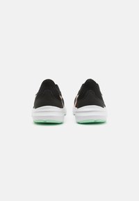 Baskets de sport noires avec semelles blanches et accents verts, présentant une texture lisse et un design minimal, conçues pour le confort et la performance.