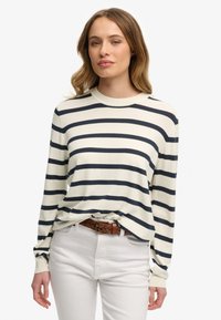 Sweter w paski z okrągłym dekoltem w kolorze kremowym z granatowymi poziomymi paskami. Miękki materiał, długie rękawy, luźny krój, zestawiony z białymi spodniami i brązowym paskiem.