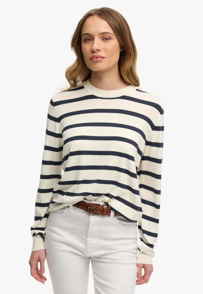 Sweter w paski z okrągłym dekoltem w kolorze kremowym z granatowymi poziomymi paskami. Miękki materiał, długie rękawy, luźny krój, zestawiony z białymi spodniami i brązowym paskiem.