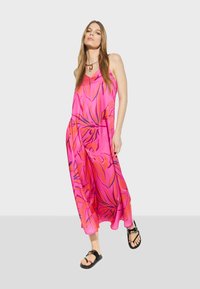 Pink floral maxi dress with spaghetti straps, featuring a loose fit, vibrant orange and blue patterns, paired with black flat sandals.