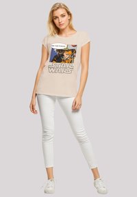 Beige T-shirt with short sleeves featuring a Star Wars graphic print in color, paired with white skinny jeans and white sneakers.