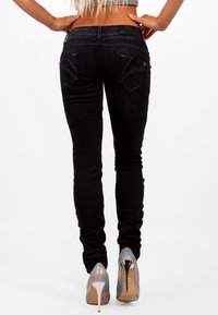 Jeans skinny neri con un design aderente, caratterizzati da rifiniture a cucitura e due tasche posteriori, abbinati a scarpe con tacco alto iridescenti.