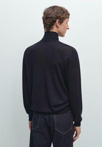 Svart polotröja med en avslappnad passform, långa ärmar och ribbade manschetter, kombinerad med mörka denimjeans. Enkel, slät textur.