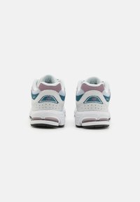 Baskets blanches avec des accents bleu-vert et mauve, col rembourré et détails perforés. Semelle en caoutchouc flexible pour traction et soutien.