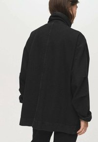 Zwarte spijkerjack met hoge kraag, losse pasvorm en verlaagde schouders. Voorzien van minimalistische naaddetails en een zachte textuur.