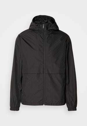 Casaco corta-vento preto com um padrão texturizado que apresenta linhas diagonais e formas de diamante subtis, fecho zip frontal completo e capuz. Punhos elásticos.