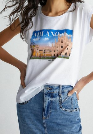 Hvid T-shirt med korte ærmer med et farverigt "Milano" grafisk tryk med arkitektoniske motiver, kombineret med en blå denims nederdel med nitter.