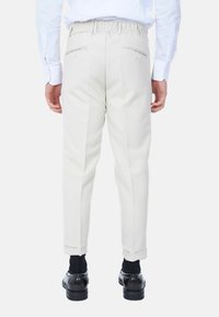 Pantaloni beige chiaro con vita elasticizzata, due tasche posteriori con zip, forma affusolata e polsini, abbinati a scarpe nere e calze.