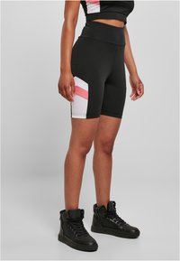 Shorts de sport noirs à taille haute, avec des rayures diagonales blanches et roses sur les côtés. Associés à des baskets montantes noires.