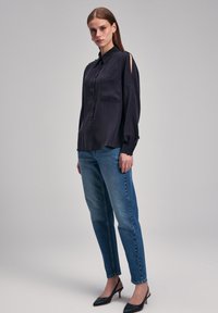 Granatowa koszula z długim rękawem, z zapięciem na guziki, z jednym kieszonkowym na piersi i bocznymi rozcięciami. Połączona z jasnoniebieskimi dżinsami prostymi i czarnymi szpilkami.