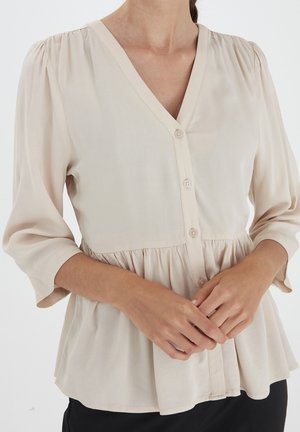 Beige peplum bluse med V-hals og trekvart lange puffærmer. Har knaplukning foran og blødt, struktureret stof.