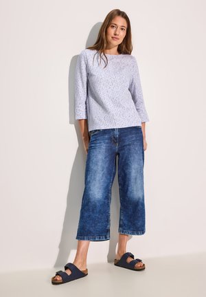 Hellblau strukturierte Bluse mit Dreiviertelärmeln, kombiniert mit weit geschnittenen, verblassten blauen Jeans und marineblauen Sandalen mit Schleifen-Detail.