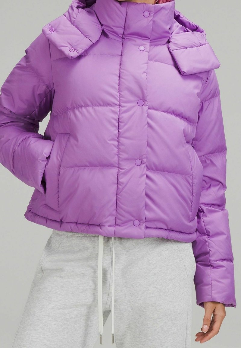 Doudoune violette avec un col montant et des boutons pression. Présente une forme carrée, des coutures plates et deux poches latérales. Texture lisse.