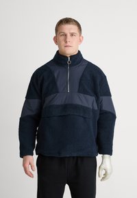 Maritieme fleece pullover met hoge kraag, ritssluiting en contrasterende stoffenpanelen. Heeft een gestructureerd oppervlak en een ontspannen pasvorm.
