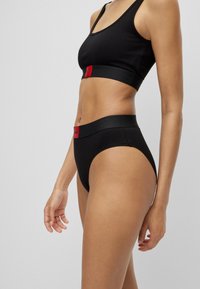 Black cotton sports bra and high-waisted brief set featuring wide elastic bands with red labels. Smooth texture, minimalistic design.