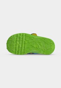 Semelle de chaussure vert vif avec des motifs d’éclaboussures ludiques, des prises texturées et le nom de la marque "superfit" embossé près du centre.