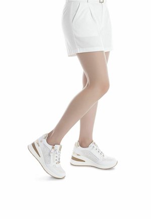 Zapatillas deportivas blancas con parte superior perforada, detalles en dorado, tacón de cuña y cierre de cordones. Incluyen cremallera lateral para facilitar el uso.