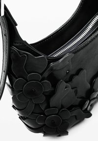 Čierna kožená taška s vystúpenými kvetinovými aplikáciami, strieborným zipsom, hladkou textúrou a zakriveným tvarom, s odnímateľným remienkom pre všestranné použitie.