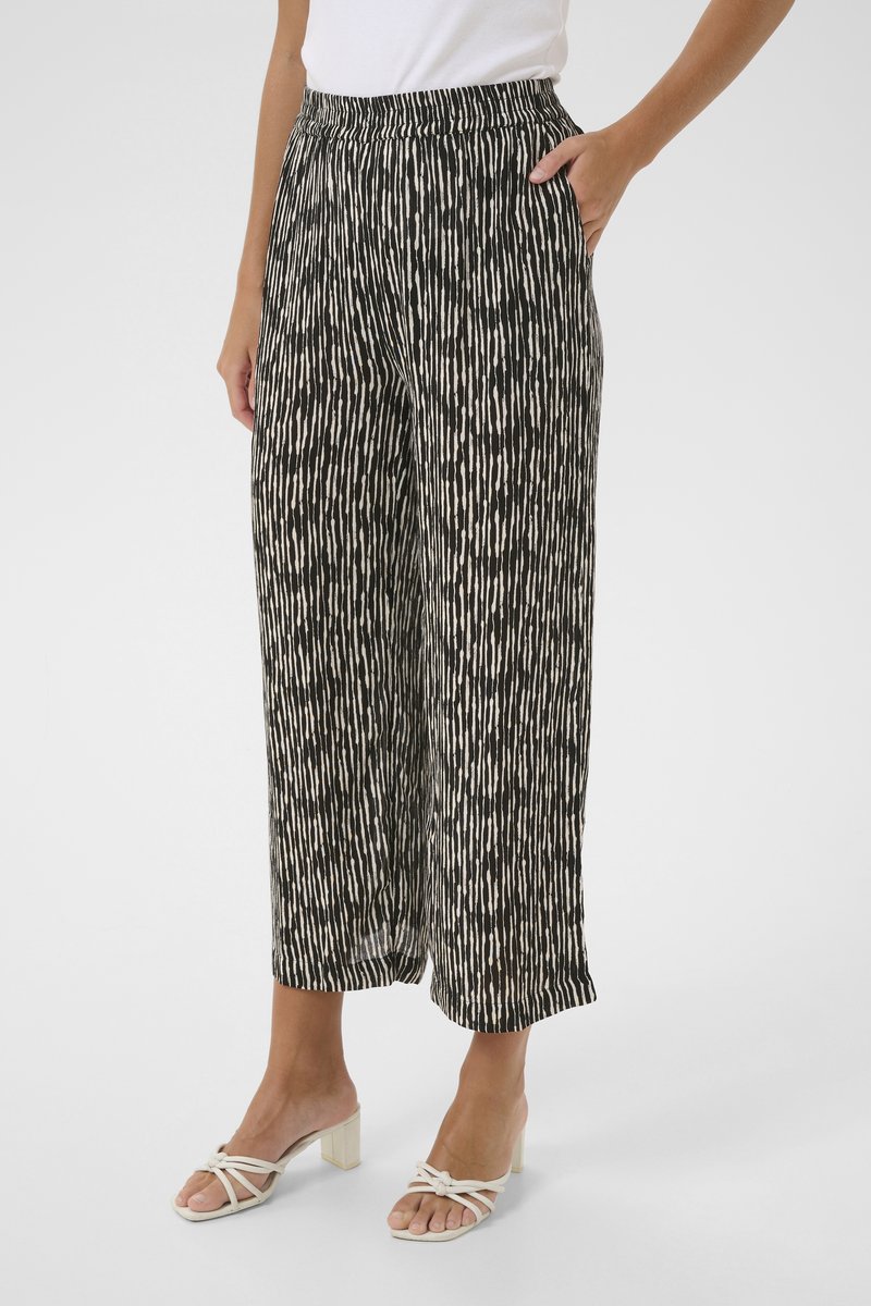 Pantalons larges à motifs noir et blanc avec une coupe décontractée, taille élastique et poches latérales, associés à des sandales à talons blocs blanches.