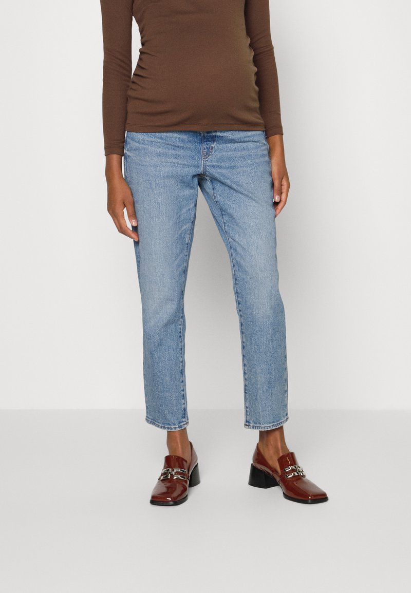 Calças de ganga azul claro com um corte reto e comprimento ligeiramente curto, combinadas com uma blusa de mangas longas castanha e mocassins castanhos brilhantes.