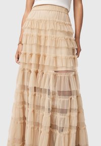 Γυμνό τούλινο μακρύ φούστα με στρώσεις από φρουφρού, ελαστική μέση και διαφανή υφή. Το μήκος της φτάνει κάτω από το γόνατο, αναδεικνύοντας έναν ρομαντικό και ρέοντα σχεδιασμό.