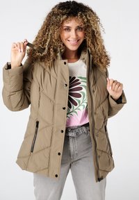 Khaki pufferjack met een doorgestikt ontwerp, zwarte knopen en zijritsen. Gecombineerd met een graphic T-shirt en grijze jeans.