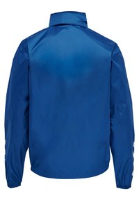 Blauwe lichtgewicht jas gezien van achteren met hoge kraag, lange mouwen, elastische manchetten en witte chevronstrepen op de onderste mouwen.