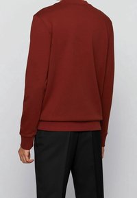 Sweatshirt bordeaux avec un col rond, des manches et un bas côtelés. Texture lisse, avec un dos uni. Associé à un pantalon noir ajusté.