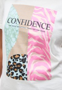 Χρωματιστό σχέδιο πατσαβούρας με μοτίβα λεοπάρδαλης, ζέβρας και πουά, και κείμενο "ΑΥΤΟΠΕΠΟΙΘΗΣΗ Το πιο όμορφο πράγμα που μπορείς να φορέσεις" σε λευκό ύφασμα.