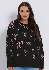 Musta neulepaita, jossa on vaaleanpunainen syd änkuvio ja -nauha, löysällä istuvuudella, pyöreällä kaula-aukolla sekä resorikynsillä ja -helmoilla. Pehmeä neulepinta.