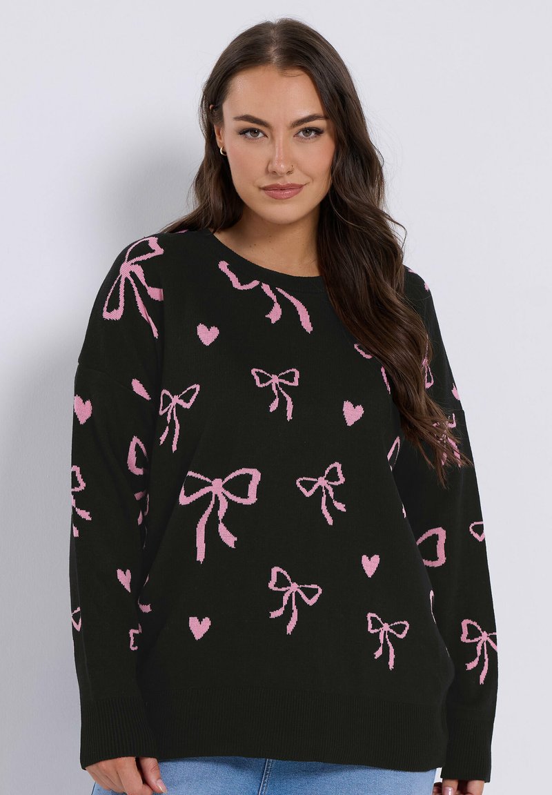 Musta neulepaita, jossa on vaaleanpunainen sydänkuvio ja -nauha, löysällä istuvuudella, pyöreällä kaula-aukolla sekä resorikynsillä ja -helmoilla. Pehmeä neulepinta.