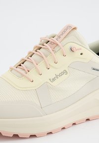 Baskets beige clair avec un dessus en maille texturée, accents roses et semelle extérieure arrondie. Présente un logo de marque et un détail résistant à l'eau.