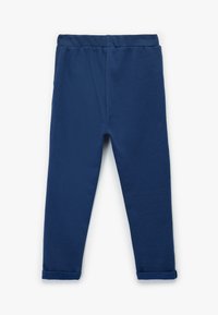 Pantalones de felpa azul marino con cintura elástica y tobillos acampanados, colocados en plano sobre un fondo blanco.