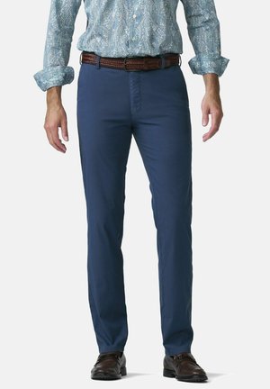 Mann trägt ein blau gemustertes langärmliges Hemd, das in marineblaue Hosen gesteckt ist, mit braunem gewebtem Gürtel und dunkelbraunen Lederschuhen.