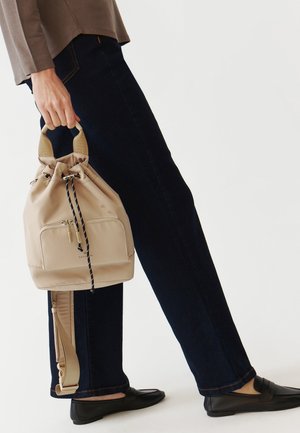 Borsa a secchiello beige con chiusura a coulisse, dotata di tasca frontale con zip e manico in tessuto con motivo a contrasto bianco e nero.
