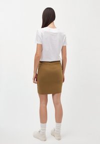 T-shirt bianco a maniche corte, gonna aderente verde oliva in maglia e sneakers crema; l'outfit presenta calze alte alla caviglia e un design semplice.