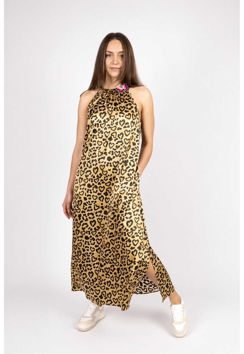 Maxikleid mit Leopardenmuster in Gold und Schwarz, mit einem Halterneck-Design und seitlichem Schlitz. Das Model trägt weiße Sneakers.