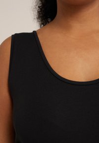 Tank top negro con escote ancho y textura acanalada, que muestra un tejido suave y un diseño ajustado. Primer plano del área del pecho.