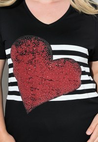 Camiseta negra con cuello en V, que presenta un gran gráfico de corazón rojo desgastado adornado con rhinestones, complementado por rayas horizontales en blanco y negro.