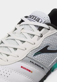 Λευκό και γκρι αθλητικό παπούτσι με λευκά κορδόνια, επάνω μέρος από δίχτυ, μαύρο λογότυπο και ετικέτες «Mundial» και «Piel» στο πλάι.