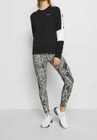 Czarna bluza z białymi akcentami i logo DKNY, zestawiona z legginsami w czarno-białym nadruku wężowym oraz białymi butami sportowymi.