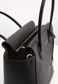 Sac à main en cuir noir à finition texturée, fermeture éclair et deux longues anses. L'intérieur est doublé de beige et présente un accent en métal doré.