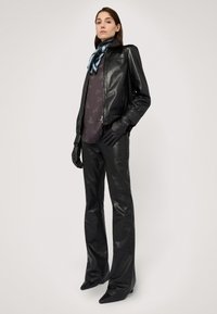 Černá kožená bunda s přiléhavým střihem, doplněná tmavým vzorovaným topem. Modelka má na sobě černé kožené rukavice a elegantní kalhoty, s špičatými botami.