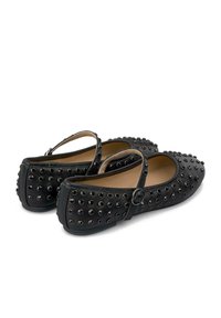 Zapatos planos negros con punta redondeada, que presentan un diseño con tachuelas y una correa ajustable en el tobillo, hechos de cuero suave.