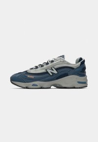 Sport shoe featuring a dark blue mesh upper with grey accents, rubber sole, reflective details, and the New Balance logo on the side.