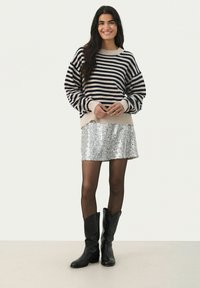 Pull en tricot rayé beige et marine, associé à une mini-jupe en sequins argentés. Des bottes noires montantes et des collants transparents complètent la tenue.